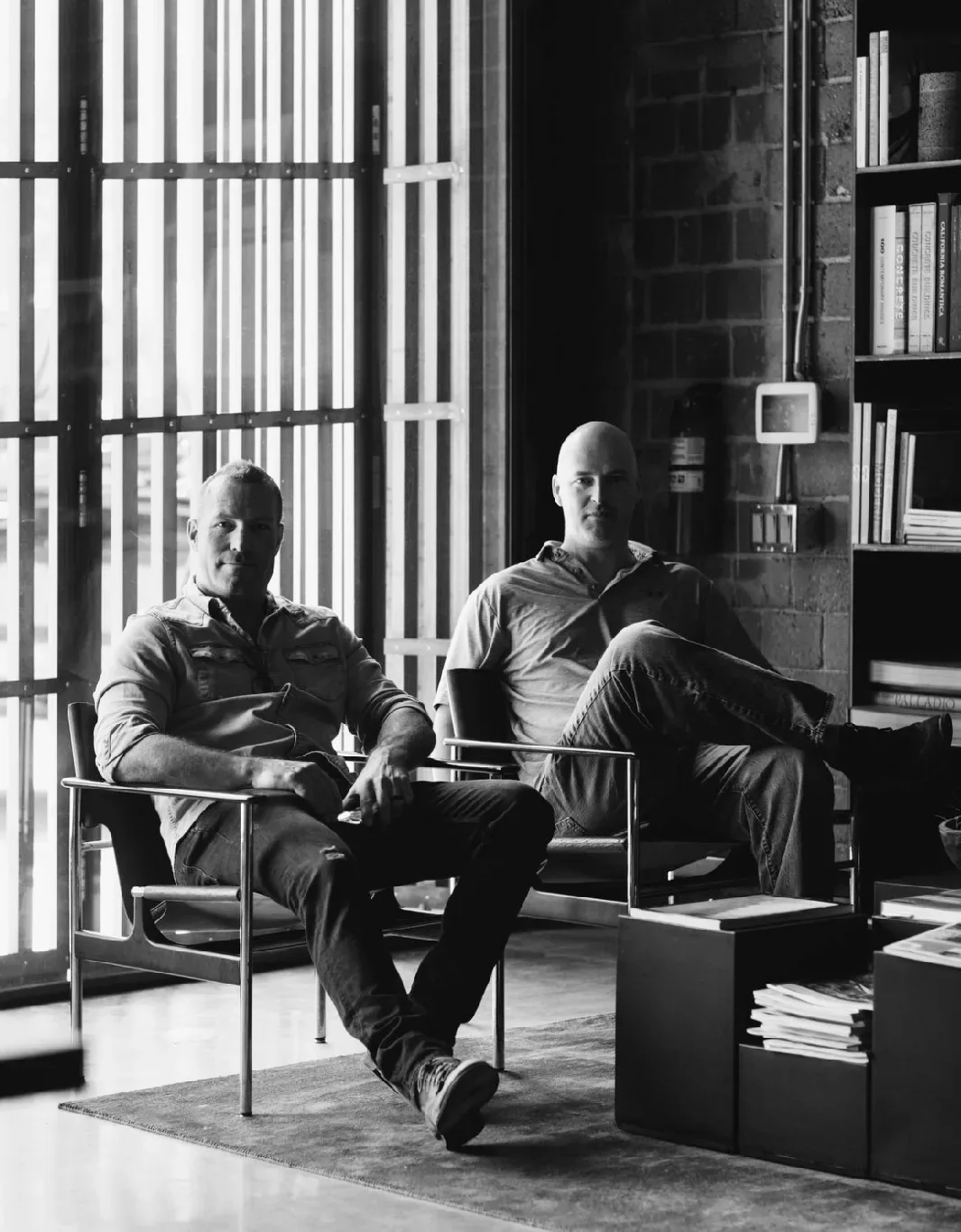 Two men sitting in chairs in front of a bookcase.